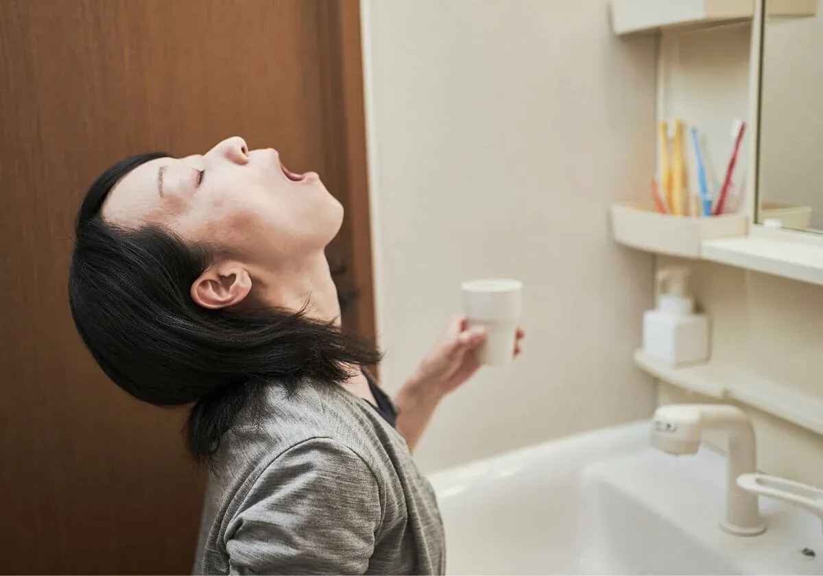 Woman gargling salt water at a bathroom sink